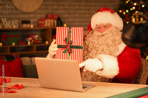 Santa Claus with laptop and Christmas gift at home