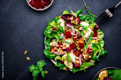 Fotografija Yummy vegan salad with beet, pear, nuts, pumpkin seeds and lettuce, black backgr