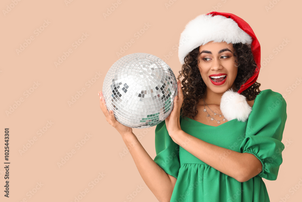 Beautiful African-American woman in Santa hat with disco ball on beige background. New Year celebration Beautiful African-American woman in Santa hat with disco ball on beige background. New Year celebration