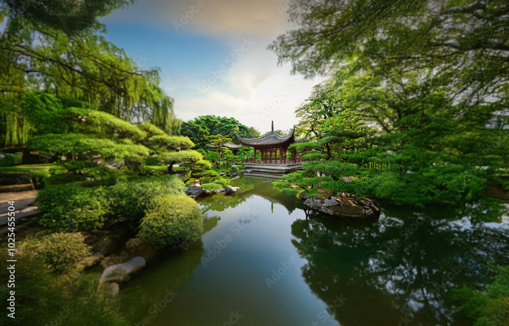 A traditional Chinese-style building with a red roof sits on the edge of a tranquil pond surrounded by lush greenery. A traditional Chinese-style building with a red roof sits on the edge of a tranquil pond surrounded by lush greenery.