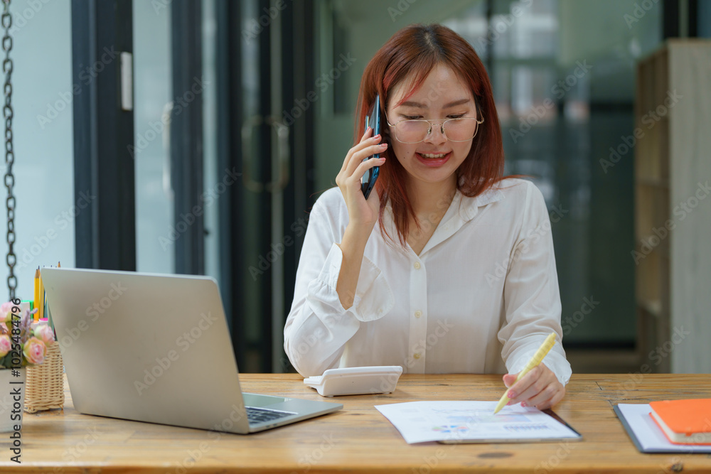 Happy, beautiful, smiling Asian businesswoman talking on a mobile phone while working in an office. Happy, beautiful, smiling Asian businesswoman talking on a mobile phone while working in an office.