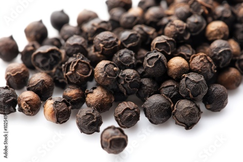 Close-up of whole black peppercorns scattered on a white surface, showcasing their glossy black texture and varying sizes.