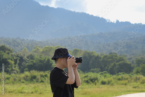 Young man traveller taking pictures of landscape in a field with mountain range in the background