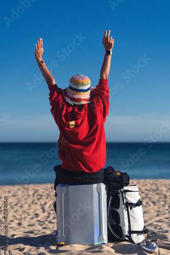 A woman travels, sits on a suitcase on the beach. photo