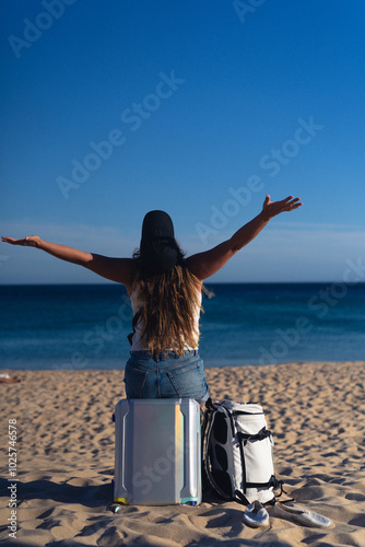 A woman travels, sits on a suitcase on the beach.