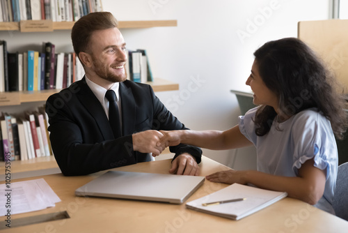 Happy Caucasian business leader man shaking hands with young Indian professional woman after work discussion, job interview, thanking for successful project, good sales result