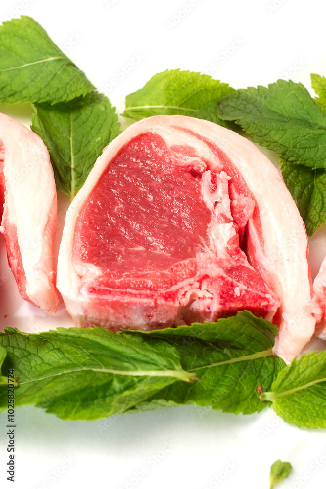 Fresh uncooked lamb loin chops and mint leaf on white background. High quality meat product cut by butcher in perfect size for cooking. Food supply chain and agriculture industry. Fresh uncooked lamb loin chops and mint leaf on white background. High quality meat product cut by butcher in perfect size for cooking. Food supply chain and agriculture industry.