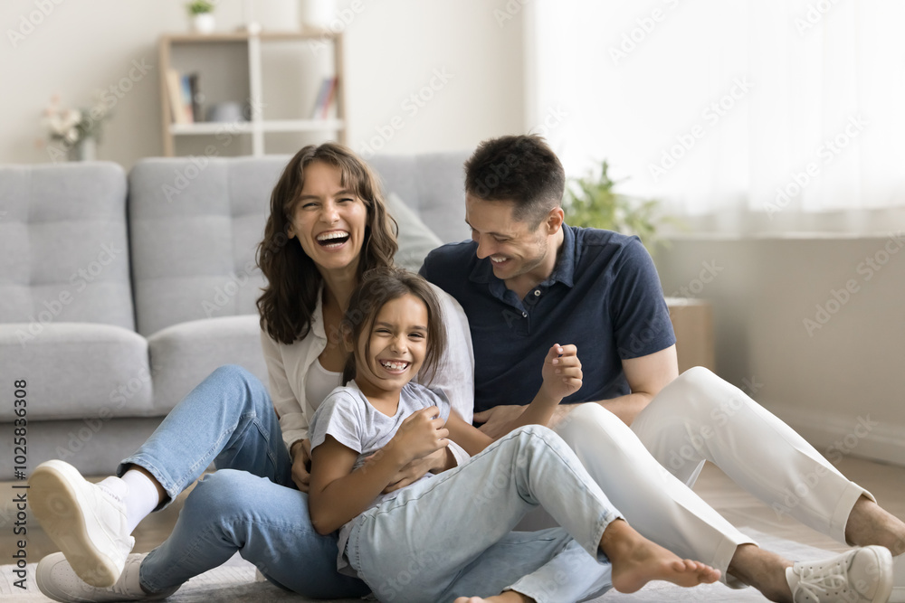 Sweet home. Laughing candid millennial spouses with preteen child mother father little daughter enjoy funny indoor activity messing tickling on floor with heating play in crazy naughty mood on weekend Sweet home. Laughing candid millennial spouses with preteen child mother father little daughter enjoy funny indoor activity messing tickling on floor with heating play in crazy naughty mood on weekend