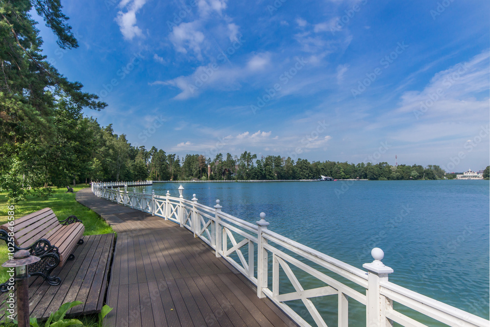 Beautiful summer landscape with a picturesque lake against the blue sky. The shore with lush greenery is decorated with a wooden embankment. Beautiful summer landscape with a picturesque lake against the blue sky. The shore with lush greenery is decorated with a wooden embankment.