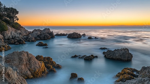 A stunning sunrise over a rocky coastline with the ocean in the background. The water is calm and the sky is a vibrant orange and pink.