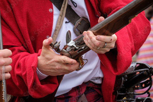 Redcoat reenactor displaying musket, demonstrating historic military weapon, musket, pistol photo