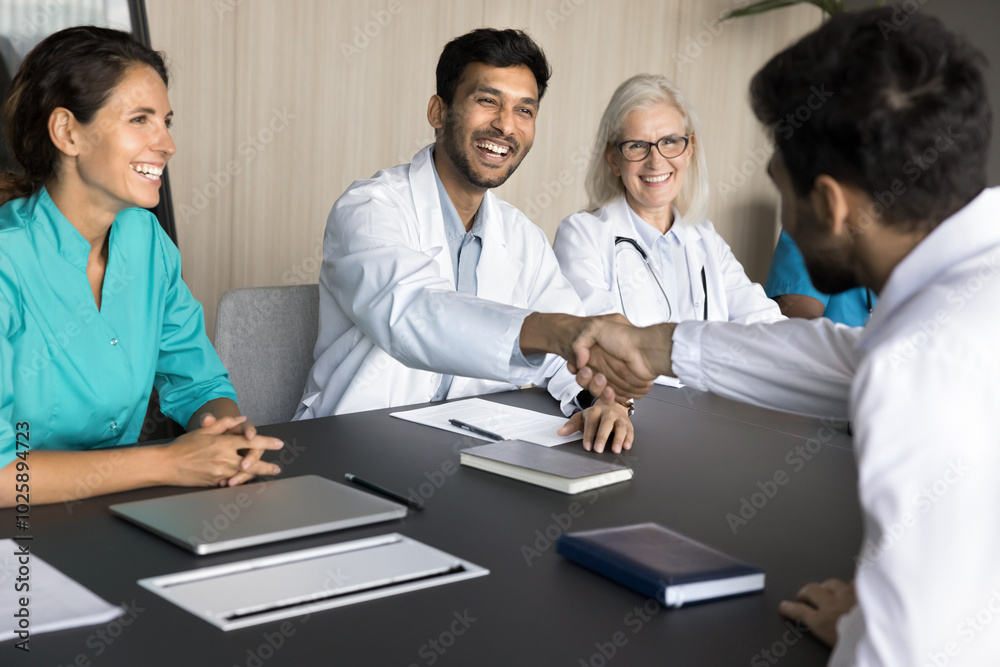 International clinic chief medical person shake hand of young male doctor congratulate new member with getting job starting career. Medic team leader handshake colleague at staff meeting show respect International clinic chief medical person shake hand of young male doctor congratulate new member with getting job starting career. Medic team leader handshake colleague at staff meeting show respect