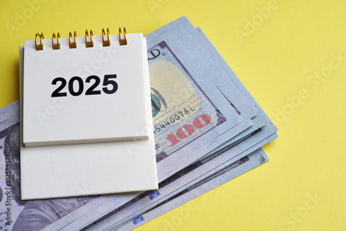 2025 calendar and dollars on yellow paper background.