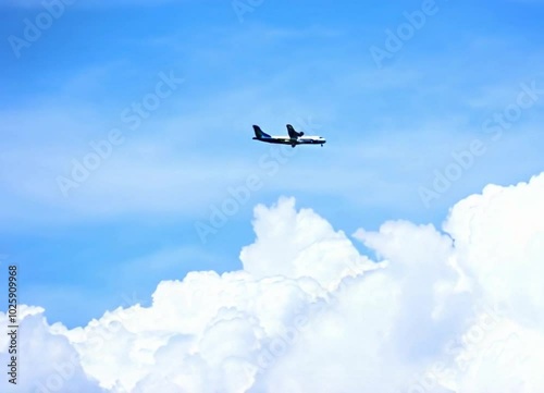 A blue and white airplane is flying through a cloudy sky. The sky is mostly blue with some white clouds scattered throughout. The airplane is the main focus of the image photo