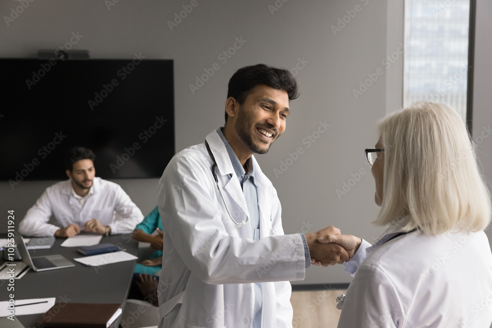 Young man doctor shake hand to senior female teammate feel gratitude for consulting good job help at hard work case. Aged woman cardiologist handshake with grateful intern student younger colleague Young man doctor shake hand to senior female teammate feel gratitude for consulting good job help at hard work case. Aged woman cardiologist handshake with grateful intern student younger colleague