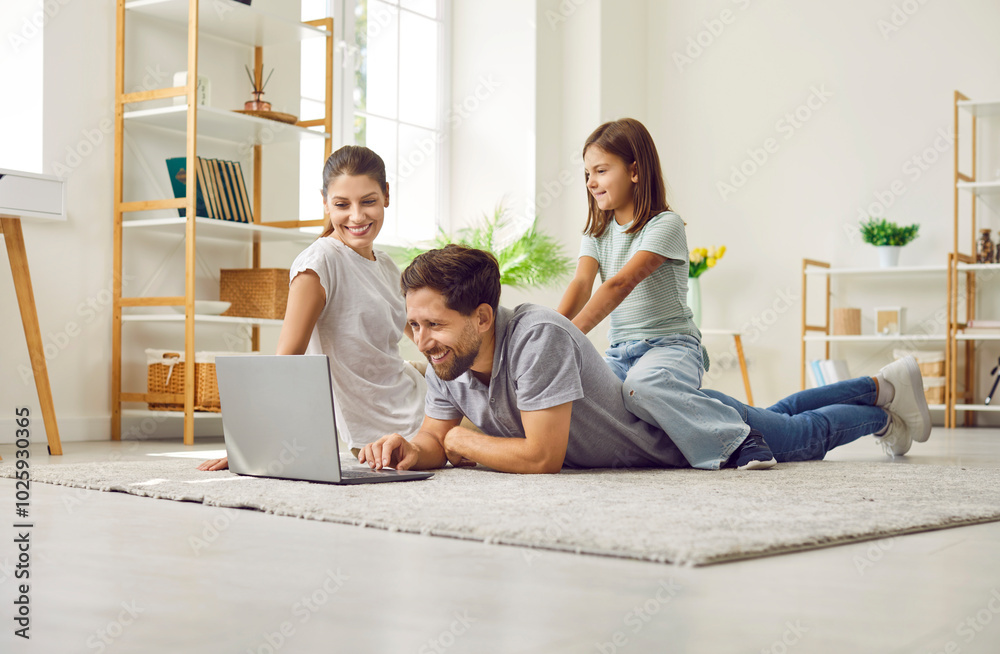 Happy family relaxing together on floor in their house or apartment, using laptop computer, shopping online, browsing holiday tickets, ordering food delivery or watching videos on streaming platform Happy family relaxing together on floor in their house or apartment, using laptop computer, shopping online, browsing holiday tickets, ordering food delivery or watching videos on streaming platform