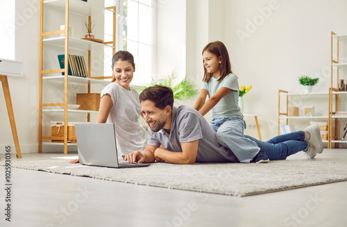 Happy family relaxing together on floor in their house or apartment, using laptop computer, shopping online, browsing holiday tickets, ordering food delivery or watching videos on streaming platform