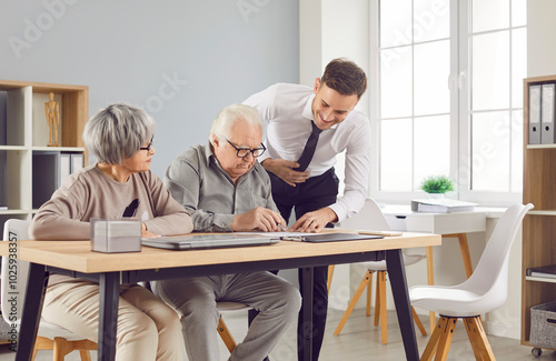 Confident gray-haired elderly senior couple sitting at the desk in office with a young man advisor or male financial agent signing a contract about health insurance or investments.