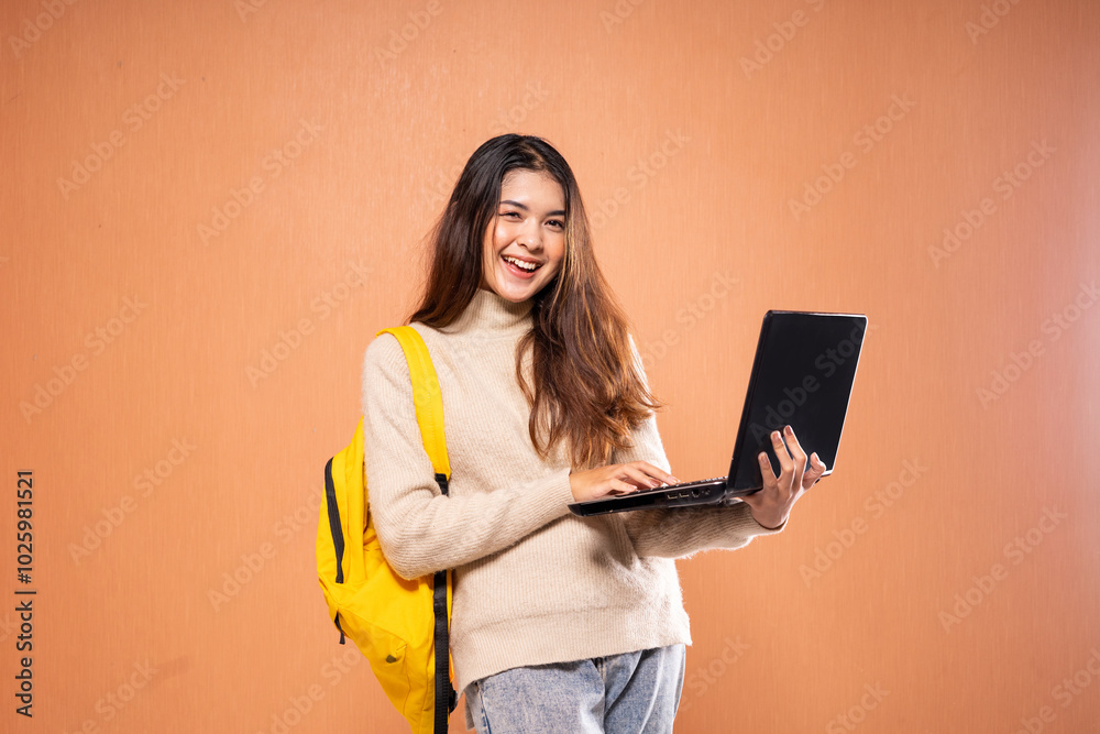 A cheerful student with long hair is happily using a laptop and wearing a yellow backpack A cheerful student with long hair is happily using a laptop and wearing a yellow backpack