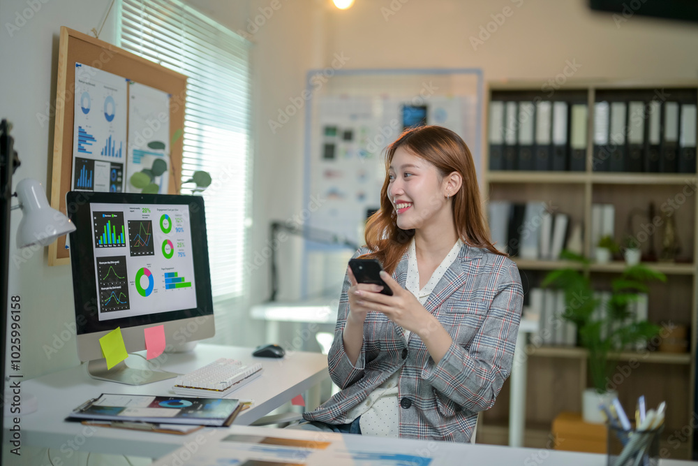A woman is sitting at a desk with a computer monitor and a cell phone A woman is sitting at a desk with a computer monitor and a cell phone