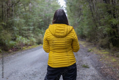 person on road between trees with yellow coat