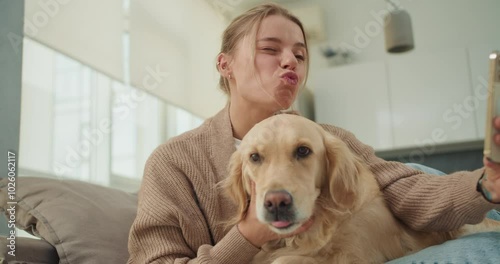 A young woman taking a selfie while playfully puckering her lips and cuddling her golden retriever, capturing a fun and heartwarming moment of bonding with her pet