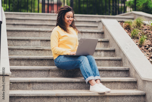 Photo of positive cute lovely girl dressed yellow stylish clothes sitting stairs in park using modern device netbook outdoors