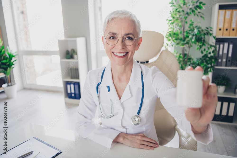Photo of aged woman qualified doctor hold give you pills jar wear white coat workplace office indoors Photo of aged woman qualified doctor hold give you pills jar wear white coat workplace office indoors