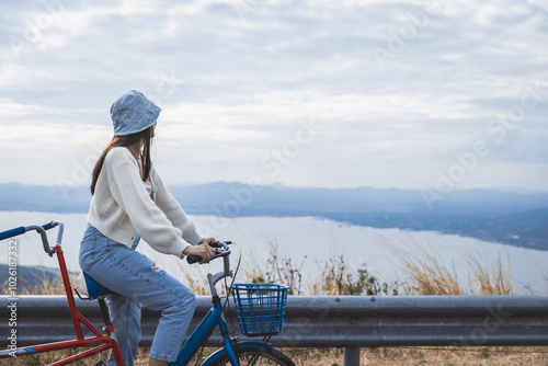 Asian woman traveler with bicycle relax and travel with wind turbine on mountain background Thailand