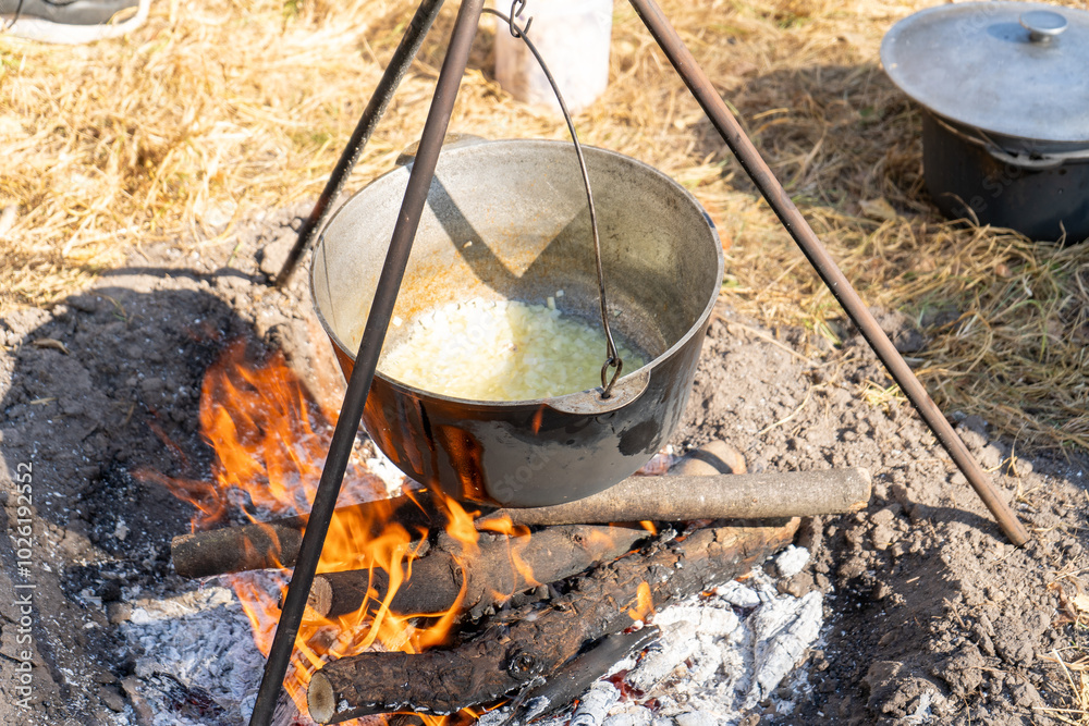 Cooking food on a campfire while hiking. Frying onion for borscht. Soup in a cauldron outdoor. Camping and summer tourism day.