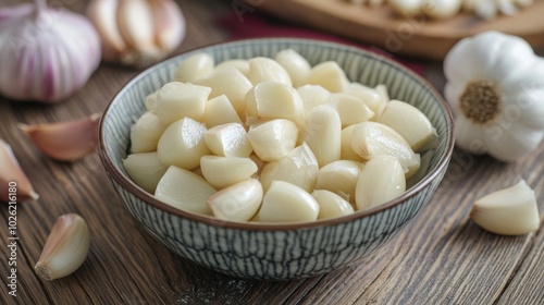 An artistic shot of a bowl filled with peeled garlic cloves on a rustic wooden table, with whole garlic bulbs nearby, emphasizing the beauty of simple ingredients.