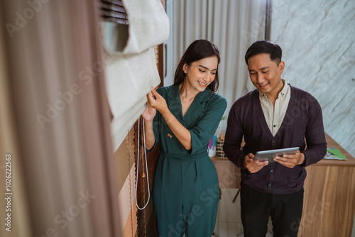 asian male shop crew showing the digital tablet to the female shop crew that tidying up the roman blinds at interior shop photo