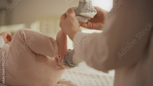 A loving parent gently puts socks on their baby's feet while the little one lies comfortably in a crib, creating a warm and nurturing atmosphere in the evening glow of their home