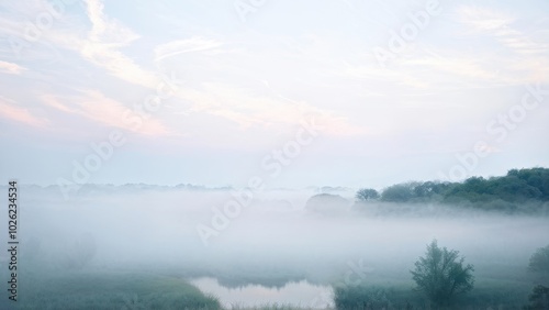 A serene landscape shrouded in morning mist, revealing a tranquil water body amidst greenery.