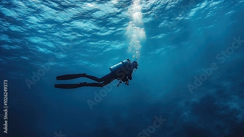 A lone scuba diver swims gracefully beneath the surface of a calm, deep blue ocean, creating a sense of adventure and peaceful exploration.