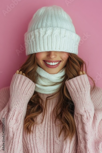 A young woman smiles while wearing a cozy sweater and winter accessories agai...