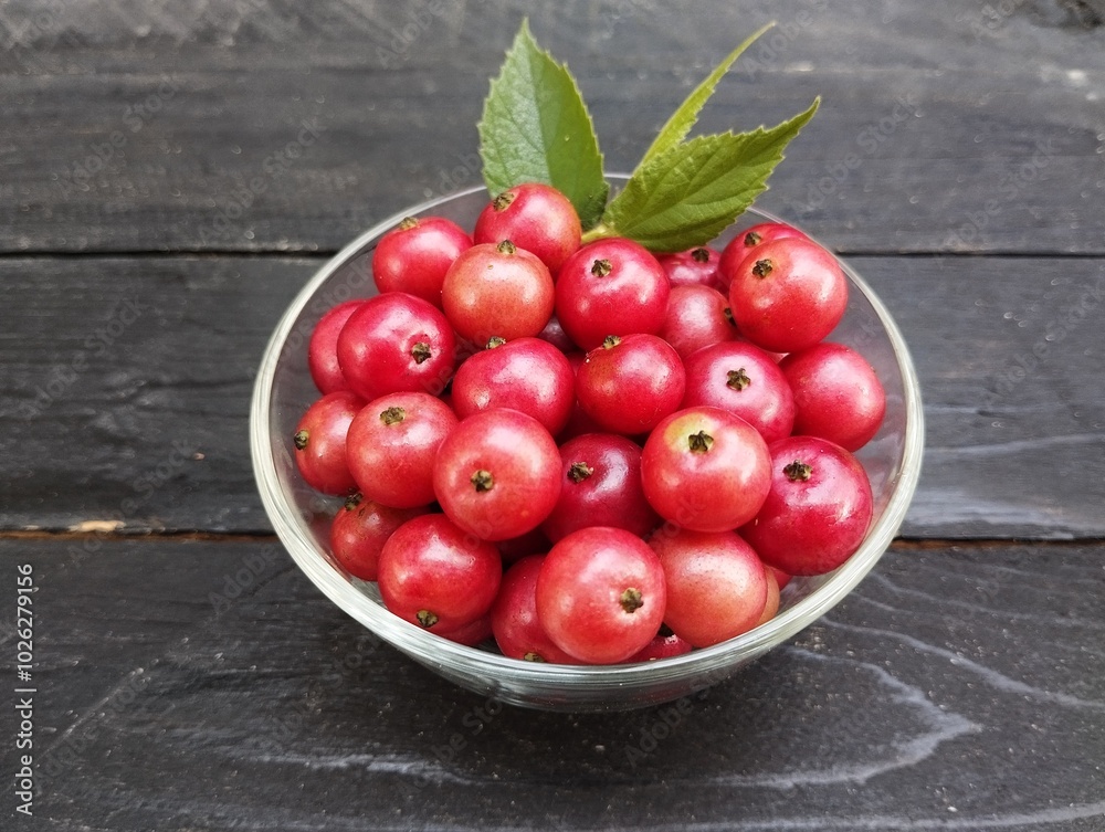 Muntingia calabura or cherries in a bowl on the black wooden table Muntingia calabura or cherries in a bowl on the black wooden table