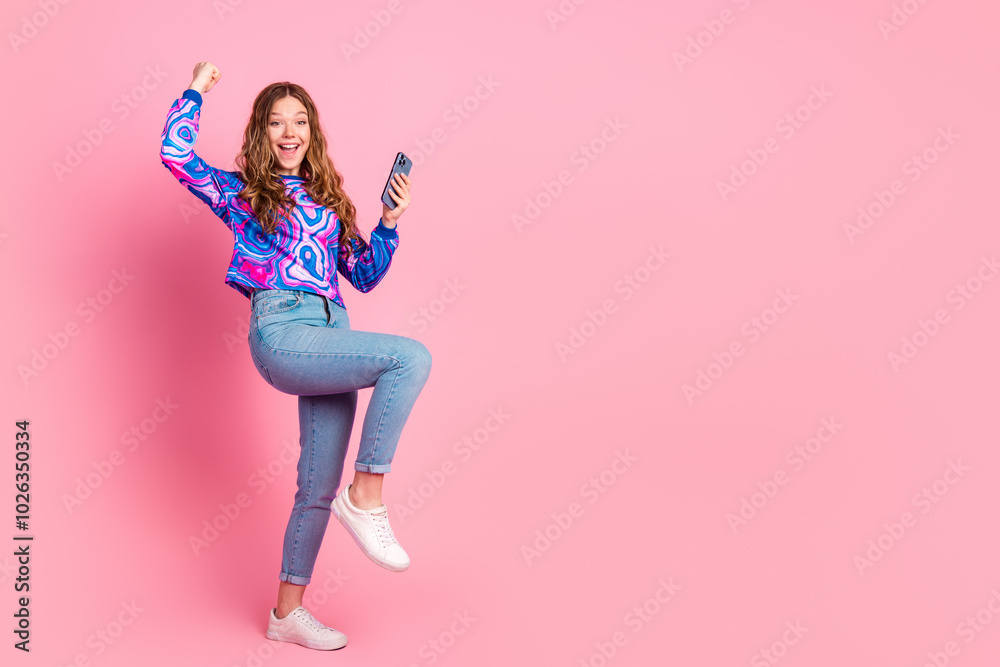 Full size photo of pretty young woman phone raise fist wear pullover isolated on pink color background Full size photo of pretty young woman phone raise fist wear pullover isolated on pink color background