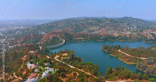 Aerial view of green hills with houses on the banks of a water reservoir with a dam in Los Angeles. Panorama of the city.