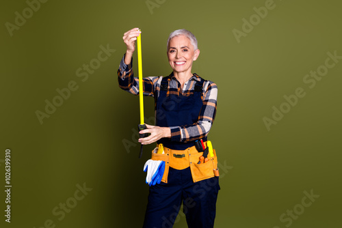Photo of attractive mature woman professional mechanic measure tape dressed blue workwear overall isolated on khaki color background