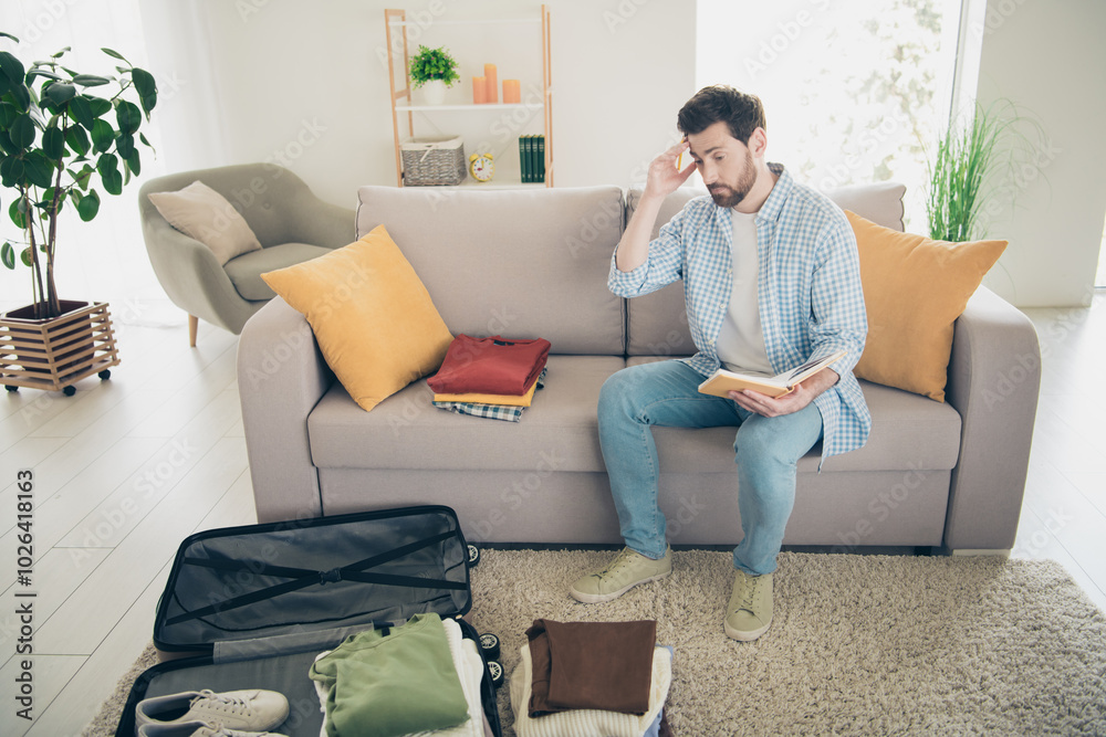 Obraz premium Photo of handsome bearded alone mature age adult man sitting indoors living room packing clothes inside valise stressed preparing for journey