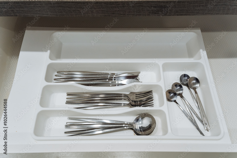A white drawer that is completely filled with various types of silverware including forks, spoons, and even scissors, all organized neatly within the confines of the drawer A white drawer that is completely filled with various types of silverware including forks, spoons, and even scissors, all organized neatly within the confines of the drawer