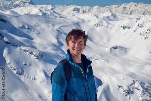 Young male skier smiling in front of a breathtaking view of snowcapped mountain peaks in the Three Valleys, France. The man is at high altitude on a sunny day in the mountaintops. photo