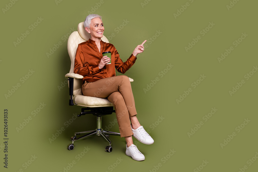 Fototapeta premium Full length photo of pensioner lady sit office armchair coffee point look empty space dressed brown formalwear isolated on khaki background