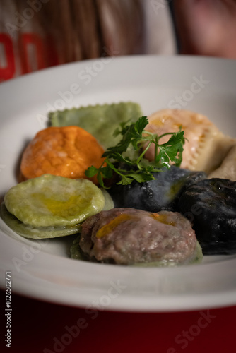 A vibrant plate of sorrentinos and ravioli showcasing different flavors and colors. The dish includes green, orange, black, and white pasta varieties, drizzled with olive oil and garnished with fresh 