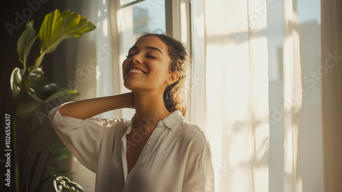 Smiling woman standing by the window, arm in hand, penetrating sun, relaxed and comfortable mood, minimalist interior. photo