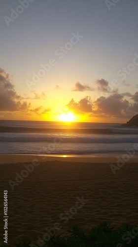 Sunrise over a sandy beach with ocean waves and a mountain silhouette in the distance.