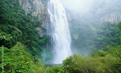 Wallpaper Mural Tilt shot with misty atmosphere: The camera starts by focusing on a tranquil waterfall cascading down a rocky cliff. The camera tilts up to reveal the mist rising from the base of the waterfall, creat Torontodigital.ca