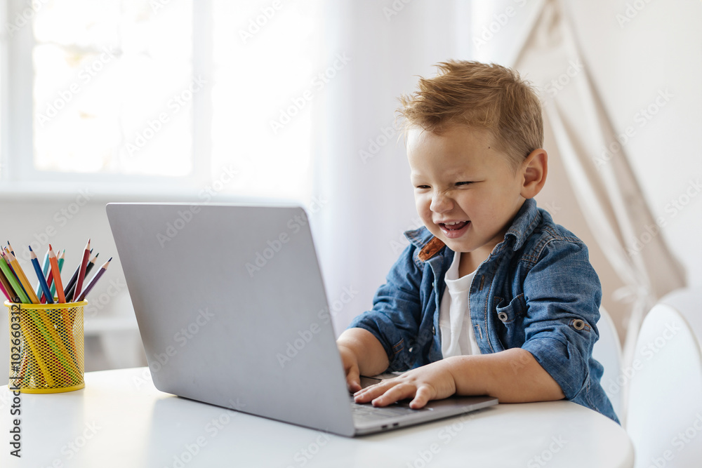 Online Education. A cheerful young boy is happily typing on a laptop, surrounded by colored pencils in a cup, enjoying a productive afternoon in a well-lit room. Online Education. A cheerful young boy is happily typing on a laptop, surrounded by colored pencils in a cup, enjoying a productive afternoon in a well-lit room.