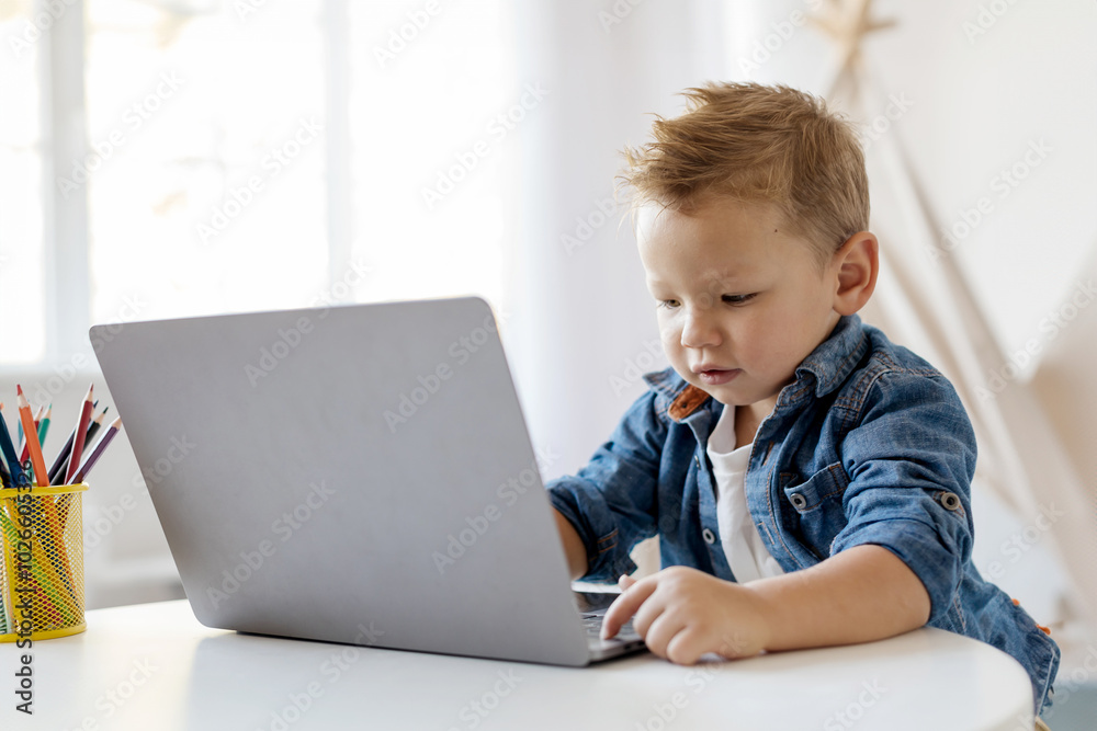 Online Education. A young boy is intently working on a laptop at a bright indoor table, surrounded by colorful pencils in a container, showcasing a moment of concentration. Online Education. A young boy is intently working on a laptop at a bright indoor table, surrounded by colorful pencils in a container, showcasing a moment of concentration.